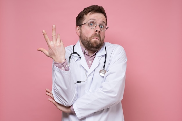 Der junge kaukasische Arzt macht verwirrt eine Handbewegung und sieht überrascht aus