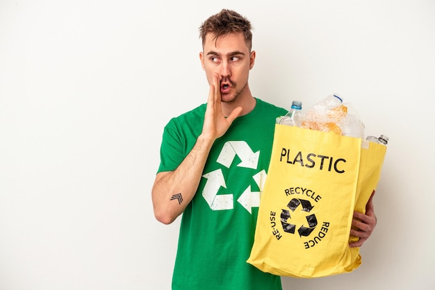 Der junge kaukasische Mann aus recyceltem Kunststoff, der auf weißem Hintergrund isoliert ist, sagt eine geheime heiße Bremsnachricht und schaut zur Seite