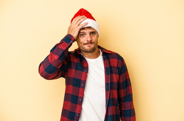 Der junge kaukasische Mann, der Weihnachten auf gelbem Hintergrund isoliert feiert, ist schockiert, sie hat sich an ein wichtiges Treffen erinnert.