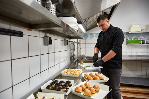 Der junge Koch in schwarzer Tunika bereitet Catering-Snacks zu