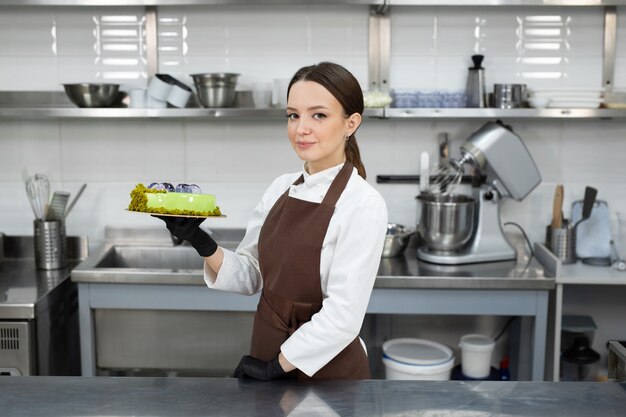 Der junge lächelnde brünette Koch hält einen Mousse-Kuchen, der mit handgemachten Pralinen verziert ist.