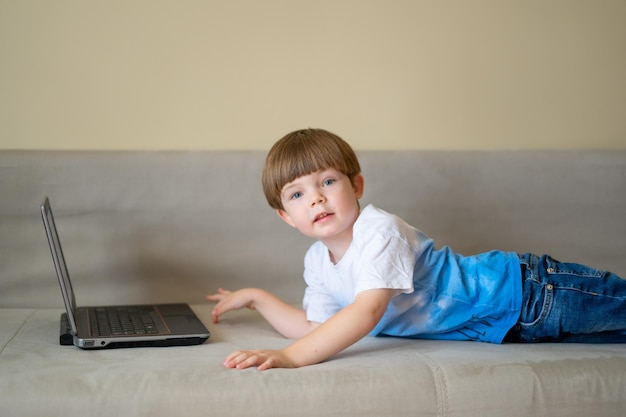 Foto der junge liegt auf einem hellen sofa und schaut auf einen laptop.