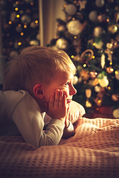 Der Junge liegt im Bett vor dem Hintergrund eines Weihnachtsbaums. Weihnachtsschmuck, warten auf den Urlaub.