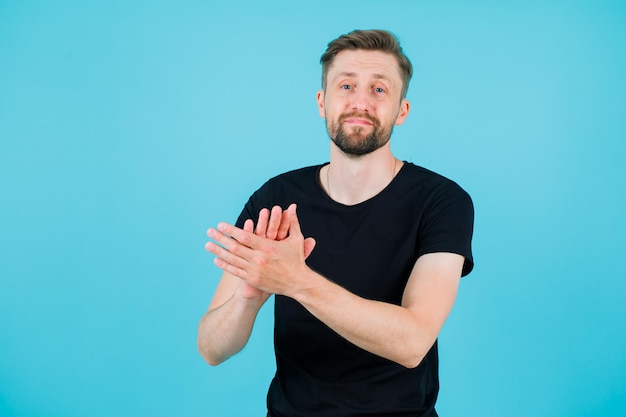 Der junge Mann applaudiert, indem er auf blauem Hintergrund in die Kamera schaut