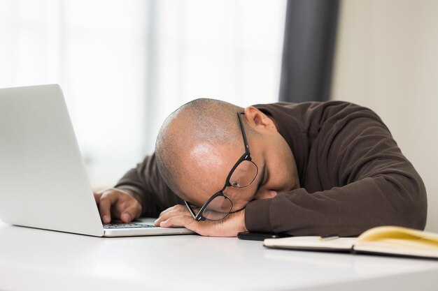 Der junge Mann arbeitete vor dem Laptop er war müde und schlief auf dem Schreibtisch ein