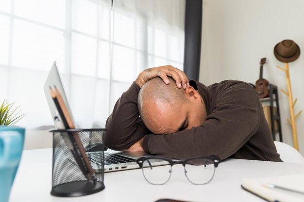 Der junge Mann arbeitete vor dem Laptop er war müde und schlief auf dem Schreibtisch ein