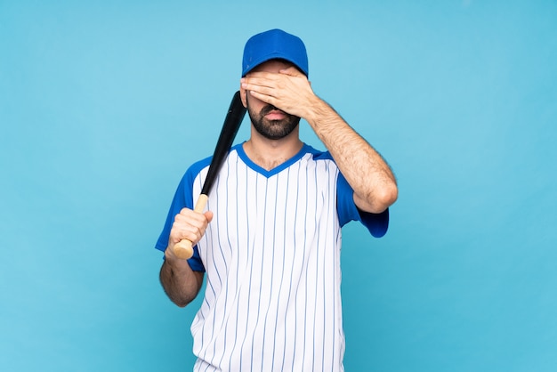 Der junge Mann, der Baseball über lokalisierter blauer Bedeckung spielt, mustert durch Hände, möchten nicht etwas sehen