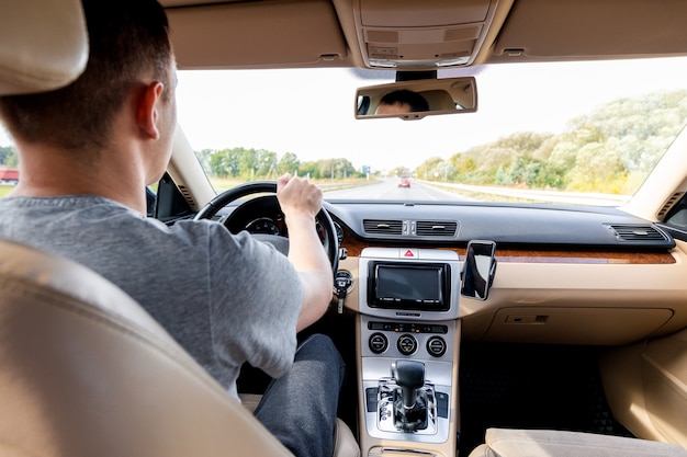 Der junge Mann, der das moderne Auto auf Asphaltstraße fährt