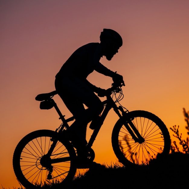 Der junge Mann, der ein Fahrrad bei Sonnenuntergang reitet