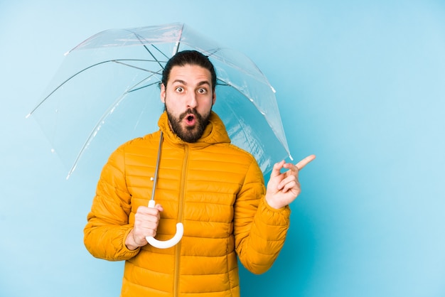 Der junge Mann, der einen langen Haarblick hält einen Regenschirm trägt, lokalisierte das Zeigen auf die Seite