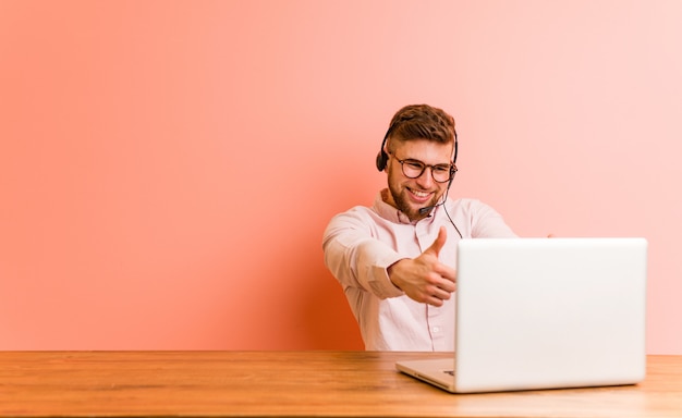 Der junge Mann, der in einem Call-Center mit den Daumen arbeitet, ups, Beifall über etwas, Unterstützung und Respektkonzept.