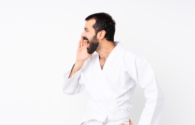 Der junge Mann, der Karate über lokalisiertem weißem Schreien mit dem breiten Mund tut, öffnen sich zur Seite