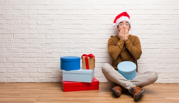 Der junge Mann, der mit den Geschenken feiert Weihnachten sitzt, erschrak sehr und ängstlich versteckt