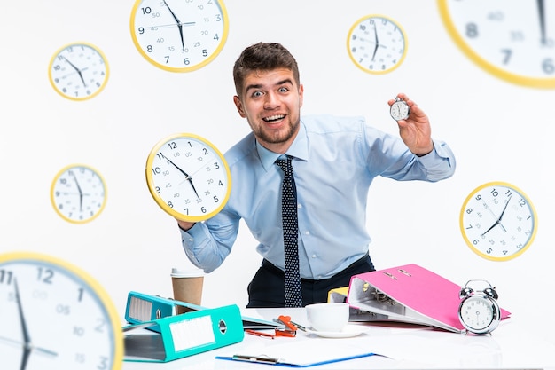 Der junge Mann kann es kaum erwarten, aus dem fiesen Büro nach Hause zu gehen. Halten Sie die Uhr und warten Sie fünf Minuten vor dem Ende. Konzept der Probleme, Geschäfte oder Probleme der Büroangestellten mit der psychischen Gesundheit.