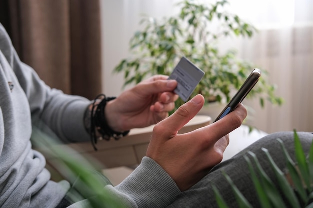 Der junge Mann kauft online auf einem Smartphone ein und sendet eine Online-Zahlung mit einer Kreditkarte