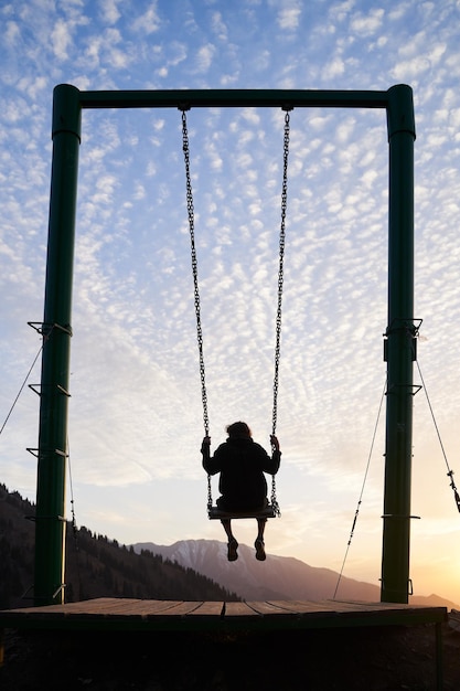 Foto der junge mann reitet während eines sonnenuntergangs auf einer schaukel in den bergen.