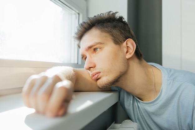 Der junge Mann schaut traurig aus dem Fenster seines Hauses, dachte er