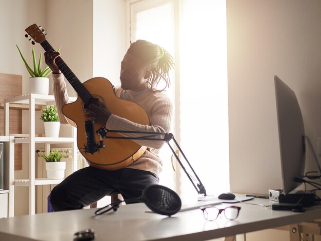 Der junge Mann singt und spielt Gitarre, während er zu Hause eine Audioaufnahme macht