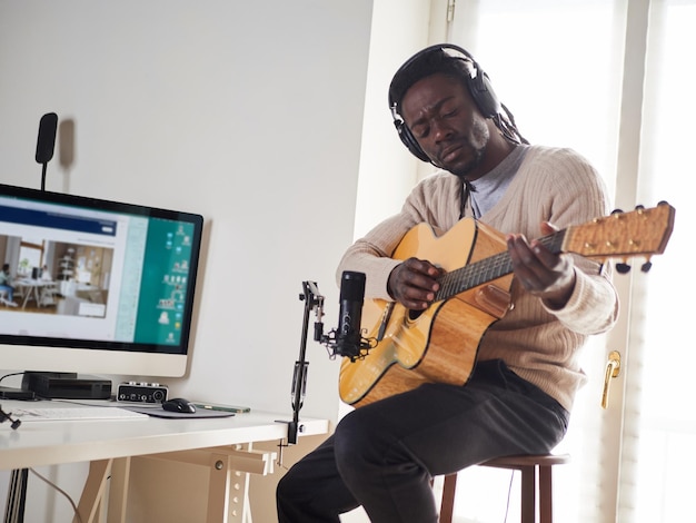 Der junge Mann singt und spielt Gitarre, während er zu Hause eine Audioaufnahme macht