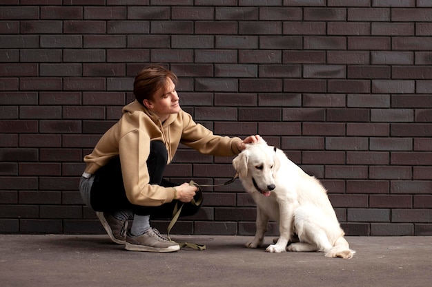 Der junge Mann sitzt mit einem Hund auf der Straße vor dem Hintergrund der Mauer