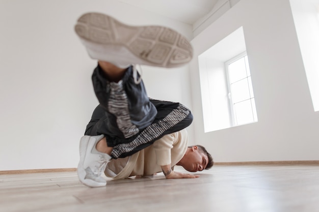 Der junge Mann steht auf einer Hand und hebt beide Beine in einem weißen Pullover und eleganten Turnschuhen an.