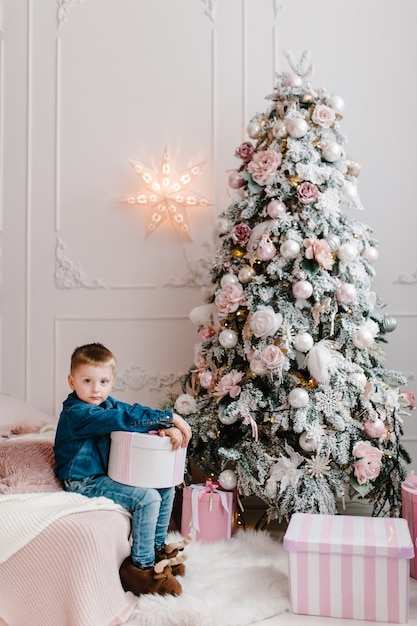 Der Junge mit Geschenken in der Nähe von Weihnachtsbaum Frohes neues Jahr und frohe Weihnachten