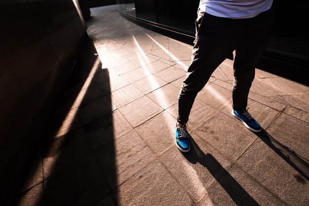 Der junge modische Kerl steht auf der Straße. Die Sonne scheint auf das Gebäude und erzeugt Glanzlichter und Schatten. Sonnenuntergang.