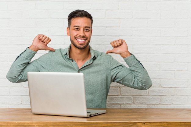 Der junge philippinische Mann, der das Arbeiten mit seinem Laptop sitzt, fühlt sich stolz und selbstbewusst, Beispiel zu folgen.