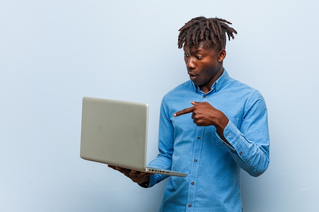 Der junge rasta schwarze Mann, der einen Laptop hält, beeindruckte das Halten des Kopienraumes auf Palme.