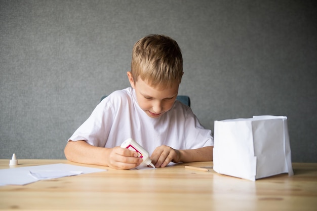 Der Junge schneidet Details aus Papier aus. Kleben Sie die Teile mit Klebstoff zusammen