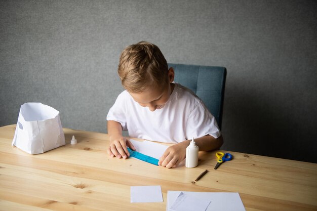 Der Junge schneidet Details aus Papier aus. Kleben Sie die Teile mit Klebstoff zusammen