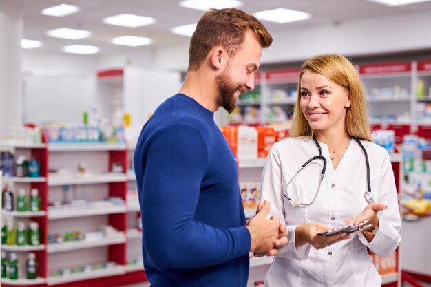 Der junge schöne kaukasische Apotheker arbeitet mit Kunden in der modernen Drogerie