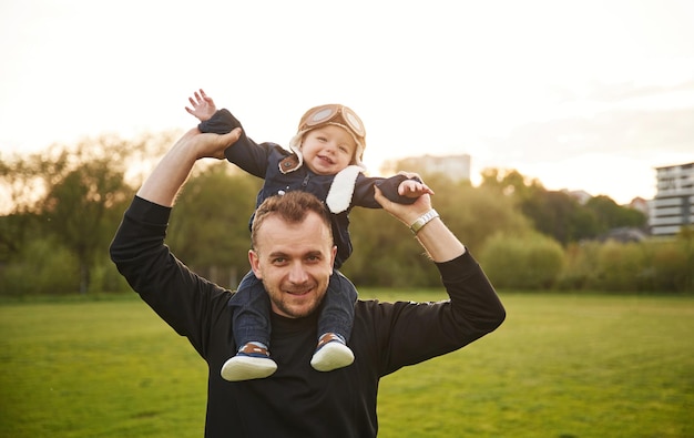 Der Junge sitzt auf den Schultern des Mannes, der Vater spielt mit seinem kleinen Sohn mit einem Spielzeugflugzeug auf dem Feld.