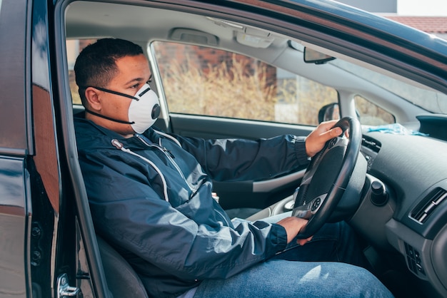 Der junge spanische Mann ist allein im Auto und trägt eine Schutzmaske