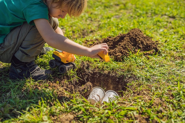 Der Junge spielt Recycling. Er vergräbt Plastik-Einweggeschirr und biologisch abbaubares Geschirr