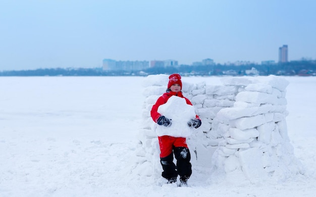 Der Junge trägt eine Schneeplatte, um ein Haus aus Schnee zu bauen