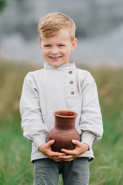 Der Junge trinkt Milch, Milch fließt durch seine Lippen. Wir haben Spaß in der Natur. Öko-Stil: Baumwolle und Leinen