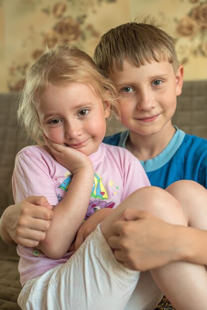 Der Junge umarmt seine kleine Schwester, die auf der Couch sitzt