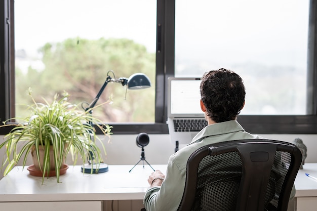 Der junge Unternehmer arbeitet von zu Hause aus in seinem Büro mit dem Computer vor einem Fenster
