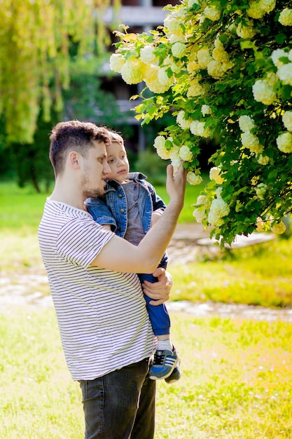 Der junge Vater und sein lächelnder Sohn umarmen sich im Park und genießen die gemeinsame Zeit beim Vatertagsfest