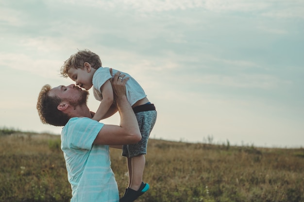 Der junge Vater wirft seinen süßen und kleinen Sohn an die frische Luft. Vatertag, Vater und sein Sohn Baby spielen und umarmen sich im Freien.