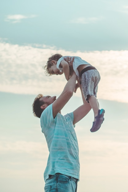 Der junge Vater wirft seinen süßen und kleinen Sohn an die frische Luft. Vatertag, Vater und sein Sohn Baby spielen und umarmen sich im Freien.