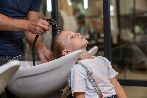 Der Junge wird seine Haare gewaschen, nachdem er sie vor einem Haarschnitt beim Friseur shampooniert hat