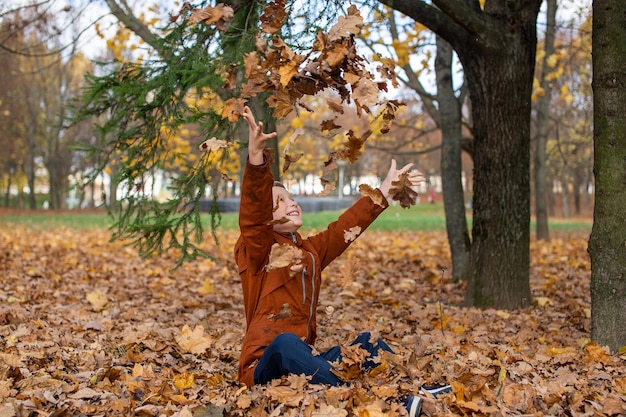 Der Junge wirft herbstgelbe Blätter, die auf ihn fliegen