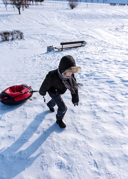 Der Junge zieht im Winter einen Schlauch