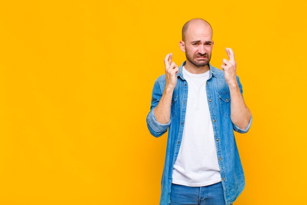 Der kahle Mann drückt ängstlich die Daumen und hofft auf Glück mit einem besorgten Blick