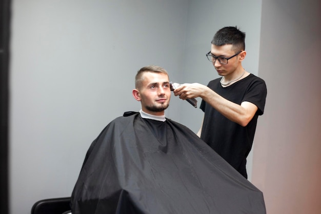 Der kasachische Friseur gibt dem Kunden einen kurzen Haarschnitt mit einem Trimmer, ein Mann hat einen Haarschnitt in einem Friseursalon