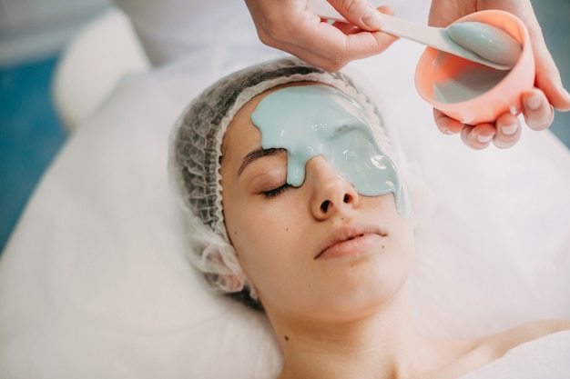 Der kaukasische Dermatologe trägt während der Spa-Behandlungen eine blaue Maske auf das Gesicht des Kunden auf
