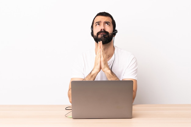 Der kaukasische Telemarketer, der mit einem Headset und mit Laptop arbeitet, hält Handfläche zusammen. Person fragt nach etwas.