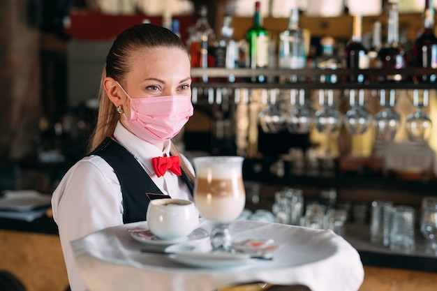 Der Kellner in einer medizinischen Maske serviert Latte-Kaffee